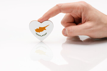 Cyprus flag. Love and respect Cyprus. A man's hand holds a heart in the shape of the Cyprus flag on a white glass surface. The concept of Cypriot patriotism and pride.