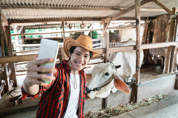 man wearing cowboy hat selfie using handphone in cow farm background