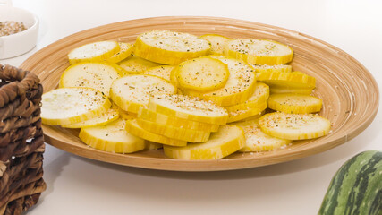 Zucchini slices with garlic seasoning and black pepper closeup on wooden plate on white background