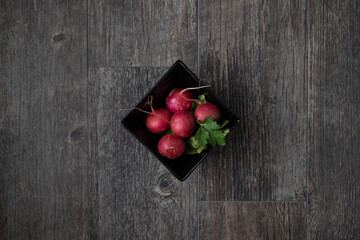 Black bowl of radishes sittin gon a wooden table
