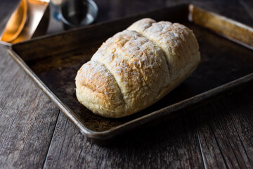 Fresh bread on a baking sheet sitting upon a wooden table top