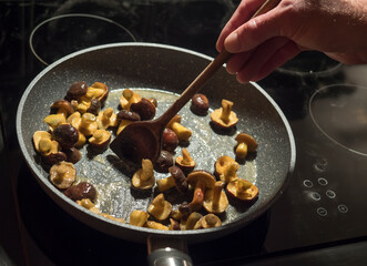 fried small whole wild boletus mushrooms. Cooking forest boletus in a pan on a hot hotplate stired with wooden spoon