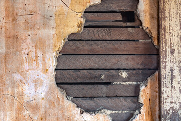 An old wall with damaged plaster, revealing the wooden lath behind the plaster. A hand print is...