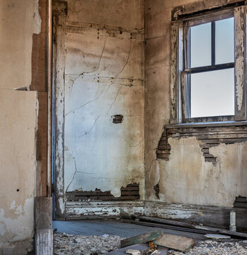 A room in an old, abandoned house with broken plaster, peeling paint and a broken window. 
