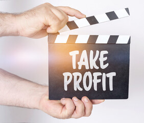 Obraz premium On a white background, a man holds a clapperboard in his hands on which it is written - TAKE PROFIT