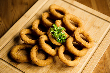 delicious golden battered, breaded and deep fried crispy onion rings served on round black stone tray on  wooden table