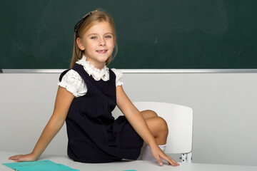 Adorable schoolgirl sitting on desk in classroom
