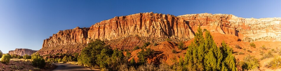 Fototapeta premium Panorama shot of stripped red sanstone mountain with green bush and road in capitol reef national park in utah, america