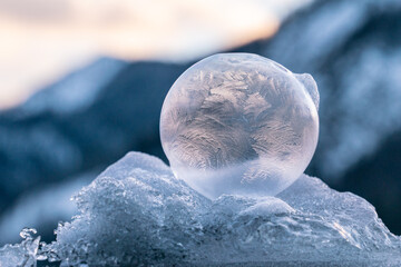 Beautiful frozen bubbles sitting on a pile of snow and ice with a delicate structure of ice flowers lit by the rising sun with mountains in the background