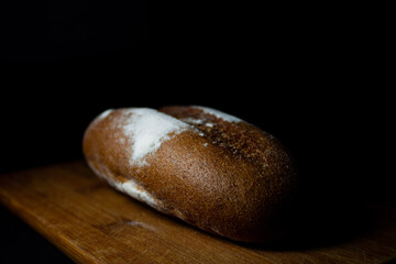 A loaf of rye black bread on a cutting board on a black background close-up.
