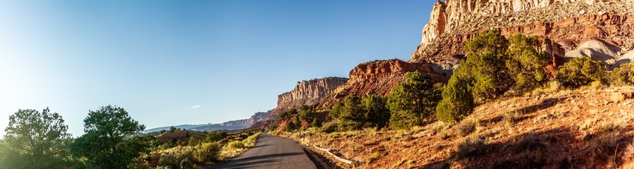 Panorama shot of stripped red sanstone mountain  with green bush and road in capitol reef national park in utah, america