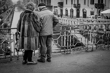 Panoramica in bianco e nero di una coppia anziana a piedi e sottobraccio che ammira dal ponte  la Darsena a Milano 