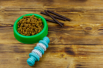 Dog toy, delicacy food and feed for dogs in green plastic bowl on wooden background. Dog care concept