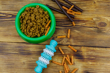 Dog toy, delicacy food and feed for dogs in green plastic bowl on wooden background. Top view. Dog care concept