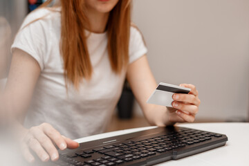 Young woman is holding credit card and using a laptop. Online shopping concept. The girl is doing e-shopping. Young woman on the sofa shopping online with debit card.