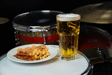 Glass of light beer with salty snacks on professional drum set closeup. Drumsticks, drums and cymbals, at live music rock concert, in the club stage, bar, or in recording studio
