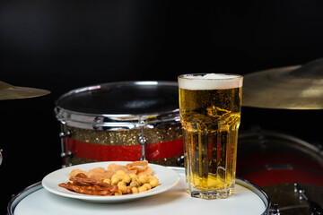 Glass of light beer with salty snacks on professional drum set closeup. Drumsticks, drums and cymbals, at live music rock concert, in the club stage, bar, or in recording studio