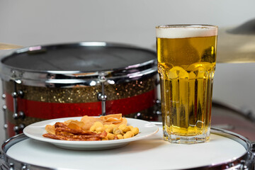 Glass of light beer with salty snacks on professional drum set closeup. Drumsticks, drums and cymbals, at live music rock concert, in the club stage, bar, or in recording studio