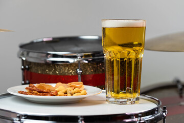 Glass of light beer with salty snacks on professional drum set closeup. Drumsticks, drums and cymbals, at live music rock concert, in the club stage, bar, or in recording studio
