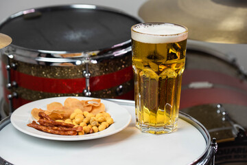 Glass of light beer with salty snacks on professional drum set closeup. Drumsticks, drums and cymbals, at live music rock concert, in the club stage, bar, or in recording studio