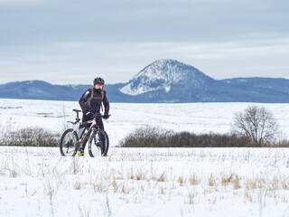 Naklejka na ściany i meble Biker is pushing mountain bike in deep snow alone. Mtb rider lost the road under snow