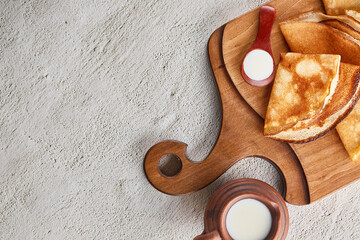 Thin pancakes on a chopping board next to a bowl of milk. Homemade pancakes and a spoonful of sour cream, traditional for Russian Maslenitsa. Thin pancake with a crisp top view with a copy space