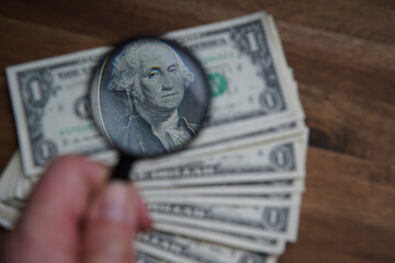 A portrait through the magnifying glass of a dollar is a portrait of the late American President George Washington. Bank image and commercial photo on brown wooden table background.