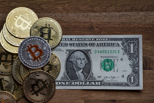 Pile of american dollars cash on brown wooden table. Next to it are several gold bitcoin digital cryptocurrency coins. Bank image and photo background.
