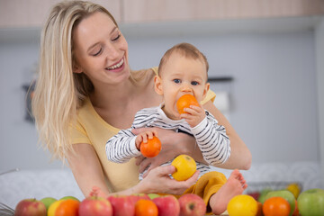 Fototapeta na wymiar mum holding baby chewing an unpeeled orange