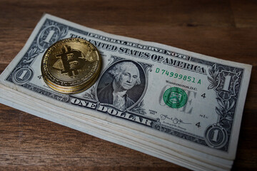 Pile of american dollars cash on brown wooden table. Next to it are several gold bitcoin digital cryptocurrency coins. Bank image and photo background.
