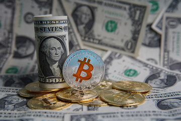 US dollars cash on the table in a money roll. Next to it are a number of gold bitcoins and a silver digital cryptocurrency coin. Bank image and commercial photo background. 