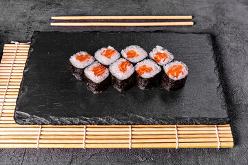 Classic Japanese sushi roll with salmon. Black background and black decor.