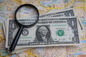 Pile of US dollar cash and a magnifying glass. European map covered with money, America with one dollar banknotes. travel concept.