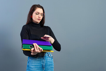 female with smartphone holding a colorfuls folders with documents, isolated on dark background