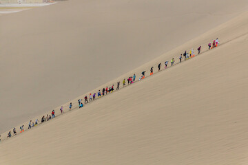 DUNHUANG, CHINA - AUGUST 21, 2018: Tourists climb Singing Sands Dune near Dunhuang, Gansu Province, China