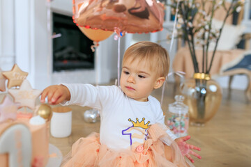 Cute baby girl celebrates birthday. One year. Close up portrait caucasian child destroys and smashes her birthday cake with butter icing getting sticky icing all over her fingers. Cake smash concept