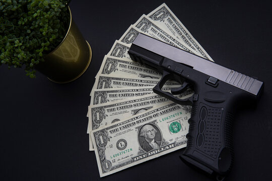 Pile of US dollar cash and a black gun. Viewed from above on a black table.