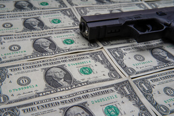 Pile of US dollar cash and a black pistol gun. Seen from above.