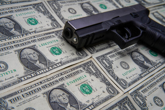 Pile of US dollar cash and a black pistol gun. Seen from above.