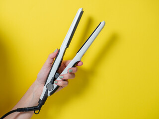 White curling iron in a woman's hand on a yellow background. An accessory for creating hairstyles....