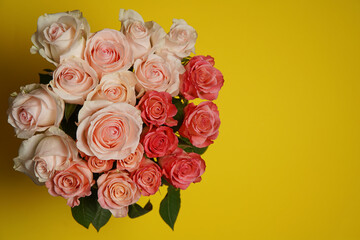 Beautiful white, red, tabby tea rose flowers in a vase photographed from above on the yellow table. Spring flowers. Wedding, mother's day and valentines day background. Selective small depth of field.