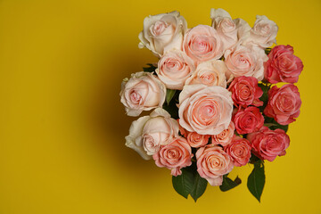 Beautiful white, red, tabby tea rose flowers in a vase photographed from above on the yellow table. Spring flowers. Wedding, mother's day and valentines day background. Selective small depth of field.