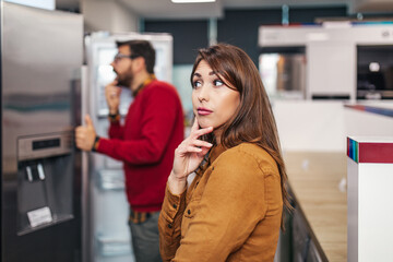 Young couple, satisfied customers choosing fridges in appliances store.