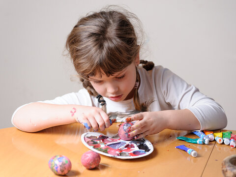 Little girl painting Easter eggs with temperas