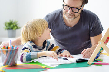 Father helping child do his homework at home. Homeschooling, distance learning, online studying, remote education for kids during quarantine is a problems for parents. Tutor teaching boy with ADHD.