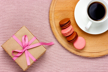 Fototapeta na wymiar Gift in a box tied with a pink ribbon. Cup of coffee and macaroon. Romantic plot.