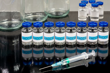 Flacons de vaccins en rangée avec reflet sur fond noir, et seringue