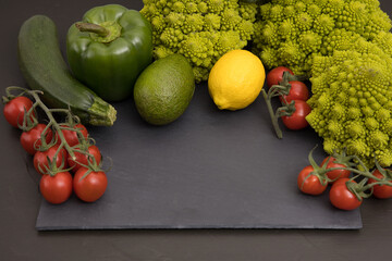 Healthy vegetarian food, fresh green food, green vegetable, romanesco broccoli, pepper, zucchini, avocado, lemon and cherry tomato, free space in you text, on a black table