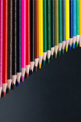 pencils in different colors slanted together with black background and copy space for free text in vertical format