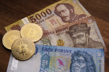 More Hungarian forint paper cash. Brown wooden table. Next to it are gold bitcoint digital cryptocurrency coin. Bank image and photo background.